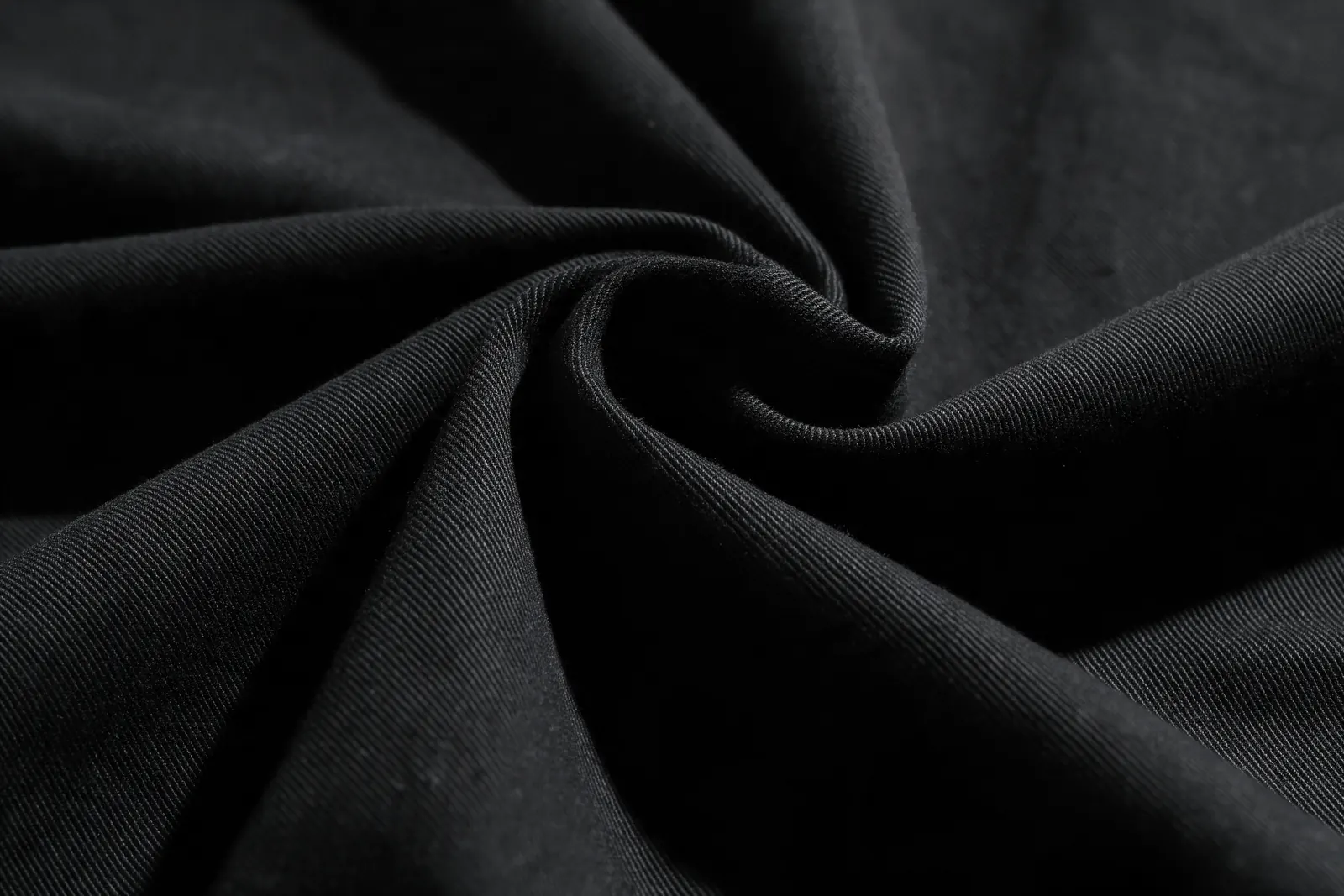 Heavy black cotton folded in a single sculptural drape under hard light.